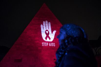 Una mujer camina cerca de la Pirámide de Cestio iluminada de rojo por el Día Mundial contra el SIDA en Roma (Italia).