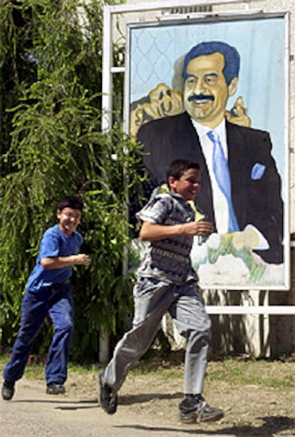 Dos niños iraquíes juegan junto a un cartel de Sadam Husein. PLANO GENERAL - ESCENA