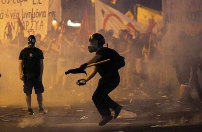 Un joven enmascarado lanza un proyectil contra los antidisturbios durante los enfrentamientos en Atenas.