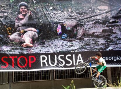 Un niño pasa con su bicicleta por una calle de Tbilisi ante un enorme cartel que reza 'detened a Rusia'.