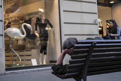 Un hombre tumbado en un banco, en el centro histórico de Roma, mira un escaparate de una tienda de ropa.