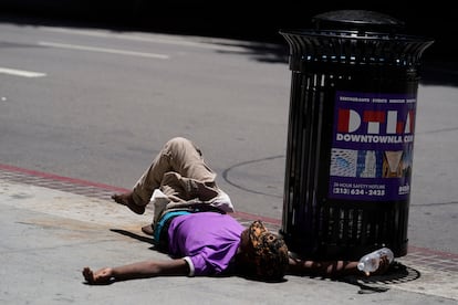 A homeless person lies on the sidewalk while holding a water bottle, Sunday, July 2, 2023, in downtown Los Angeles.