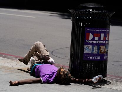 A homeless person lies on the sidewalk while holding a water bottle, Sunday, July 2, 2023, in downtown Los Angeles.