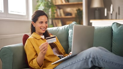 Una chica comprando en el sofá de su casa con un portátil.