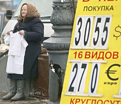 Una ciudadana de Moscú vende ropa delante de un cartel con las cotizaciones del euro y del dólar.