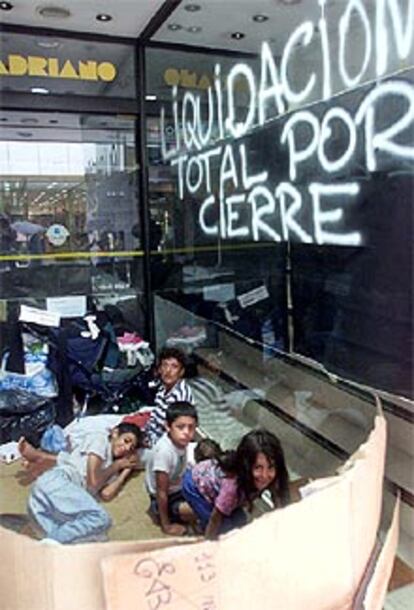 Una familia se refugia a la entrada de una tienda que anuncia su cierre.