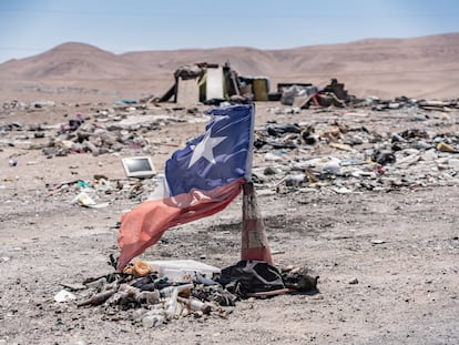 Una bandera chilena se alza en un cono de tráfico entre montones de ropa quemada en el desierto de Atacama.