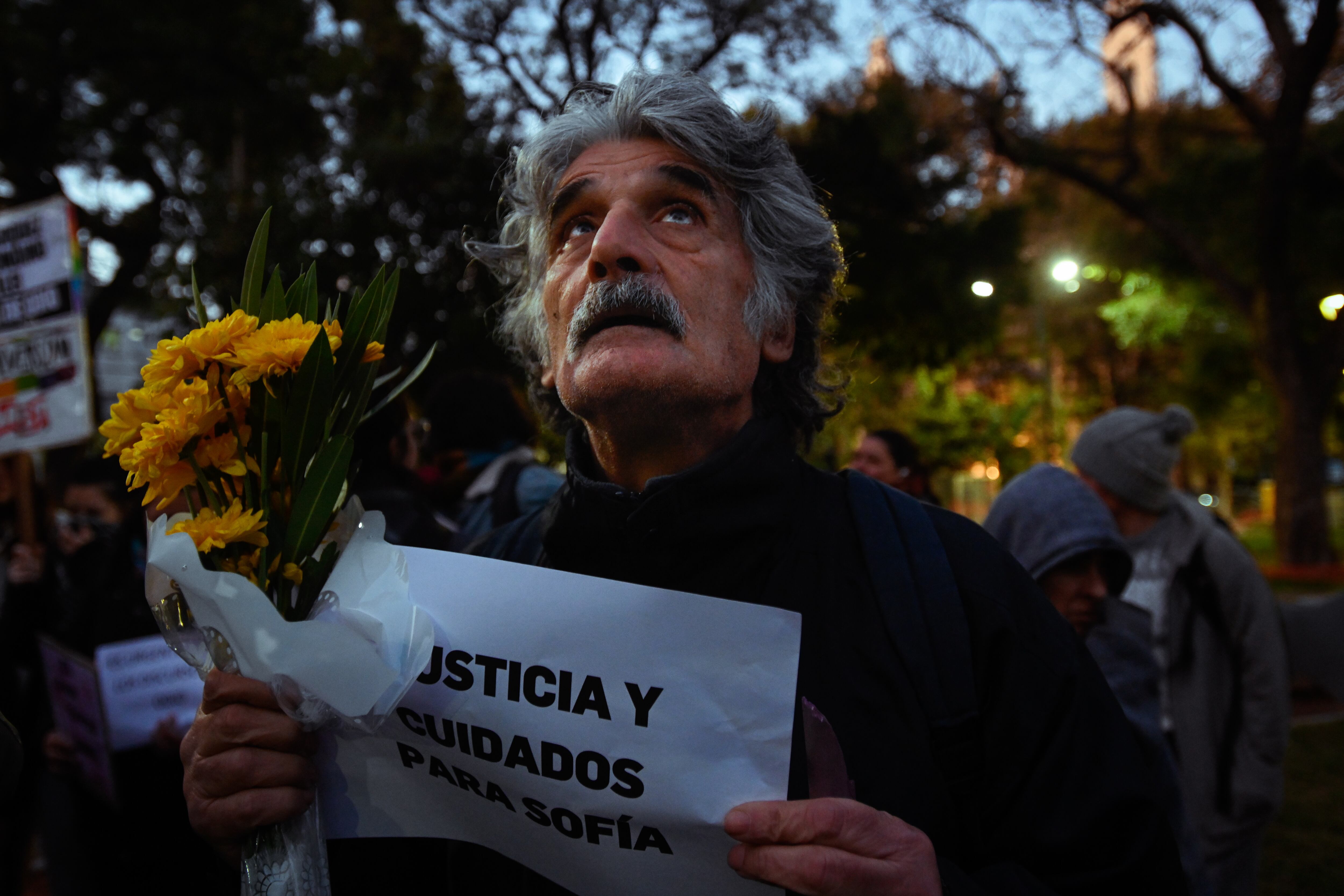 Un hombre sostiene flores y un cartel demandando justicia para las asesinadas y cuidados para la sobreviviente del ataque.