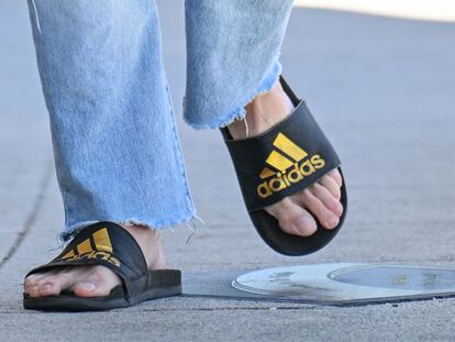 Una persona caminando por la calle con chanclas Adidas.