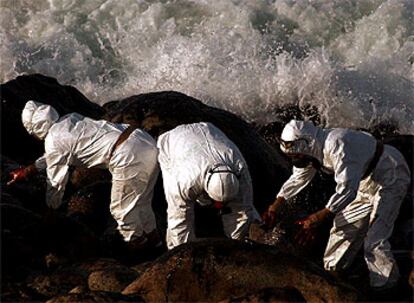 Tres voluntarios retiran fuel pegado a rocas de la localidad de Muxía (A Coruña).