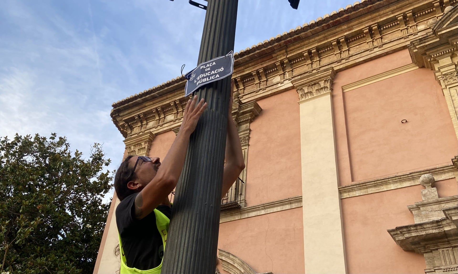 Un profesor coloca una cartel en una farola de la plaza de la Virgen de Valencia.