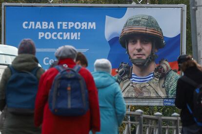 Varias personas en una parada de tranvía, frente a un cartel que mostraba este miércoles a un soldado ruso con la leyenda “Gloria a los héroes de Rusia”, en San Petersburgo.