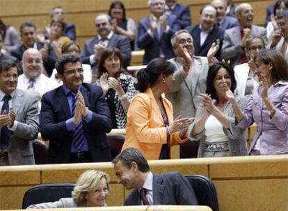 Elena Salgado y Zapatero hablan mientras aplaude la bancada de los senadores socialistas.