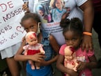 Children holding dolls covered with fake blood stand next to a sign that reads in Portuguese "Stop killing our children. We love you" during a protest against the killing of Emily Victoria Silva dos Santos, 4, and Rebeca Beatriz Rodrigues dos Santos, 7, in Duque de Caxias, Rio de Janeiro state, Brazil, Sunday, Dec. 6, 2020. The girls were killed by stray bullets while playing outside their homes. (AP Photo/Bruna Prado)