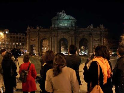 Un grupo de personas observa la Puerta de Alcalá de Madrid a oscuras durante el apagón.