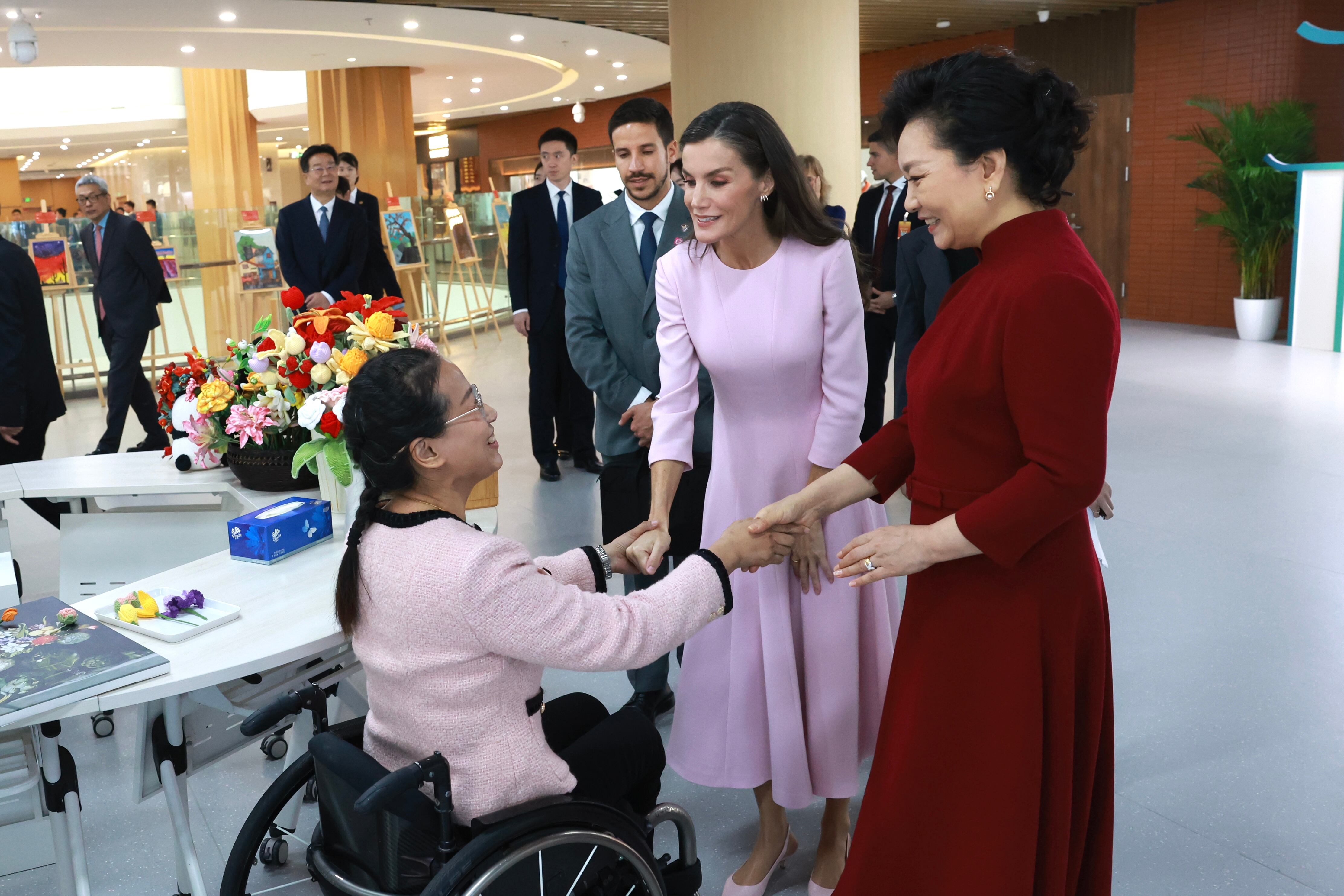La reina Letizia y Peng Liyuan saludan a Xixi durante la visita al centro para personas con discapacidad Huiai, en Pekín.