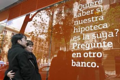 Una pareja observa el anuncio de una hipoteca situado en el exterior de una oficina bancaria.