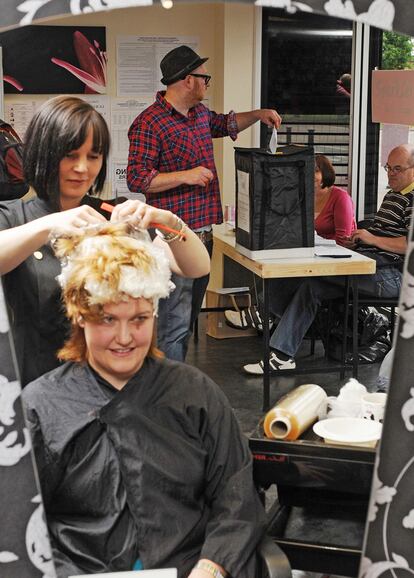 Una mujer se corta el pelo mientras un hombre emite su voto en una peluquería.