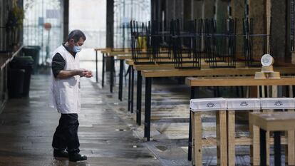 Un hombre camina junto a las mesas de varios locales vacíos por las restricciones para combatir la covid, en la plaza de abastos de Compostela.