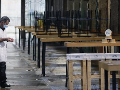 Un hombre camina junto a las mesas de varios locales vacíos por las restricciones para combatir la covid, en la plaza de abastos de Compostela.