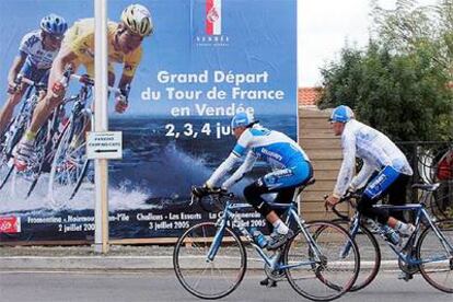 Dos ciclistas pasan en su entrenamiento por delante de un cartel anunciador del Tour.