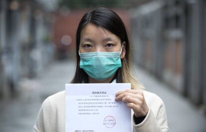 Una joven de Shanghái muestra la autorización oficial para adquirir las cinco mascarillas que el Gobierno ha destinado a cada familia.