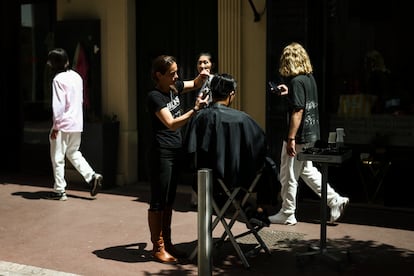 Una peluquera corta el pelo a un cliente en la calle debido a la falta de luz en el local.