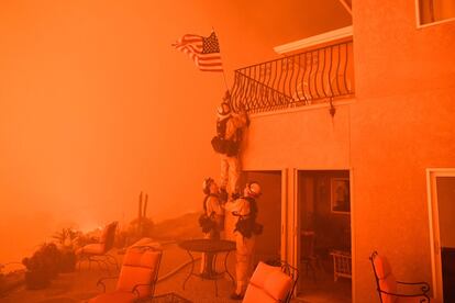 Bomberos retiran una bandera de Estados Unidos de una lujosa casa en Oroville, California, mientras el fuego se acerca al recinto, el 8 de julio de 2017.