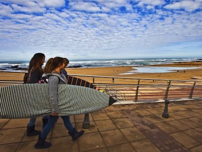 Surferas en la playa de Sopelana, el caser&iacute;o de Landetxo y una fila de copas de vino preparadas para una cata de chacol&iacute;.