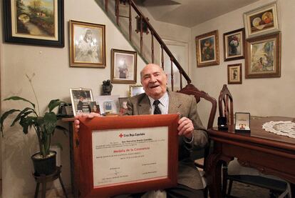 Marcelino Martín en el salón de su casa con el diploma del premio a la Constancia; encima de la mesa, las dos medallas de la Cruz Roja.