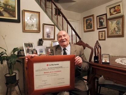 Marcelino Martín en el salón de su casa con el diploma del premio a la Constancia; encima de la mesa, las dos medallas de la Cruz Roja.