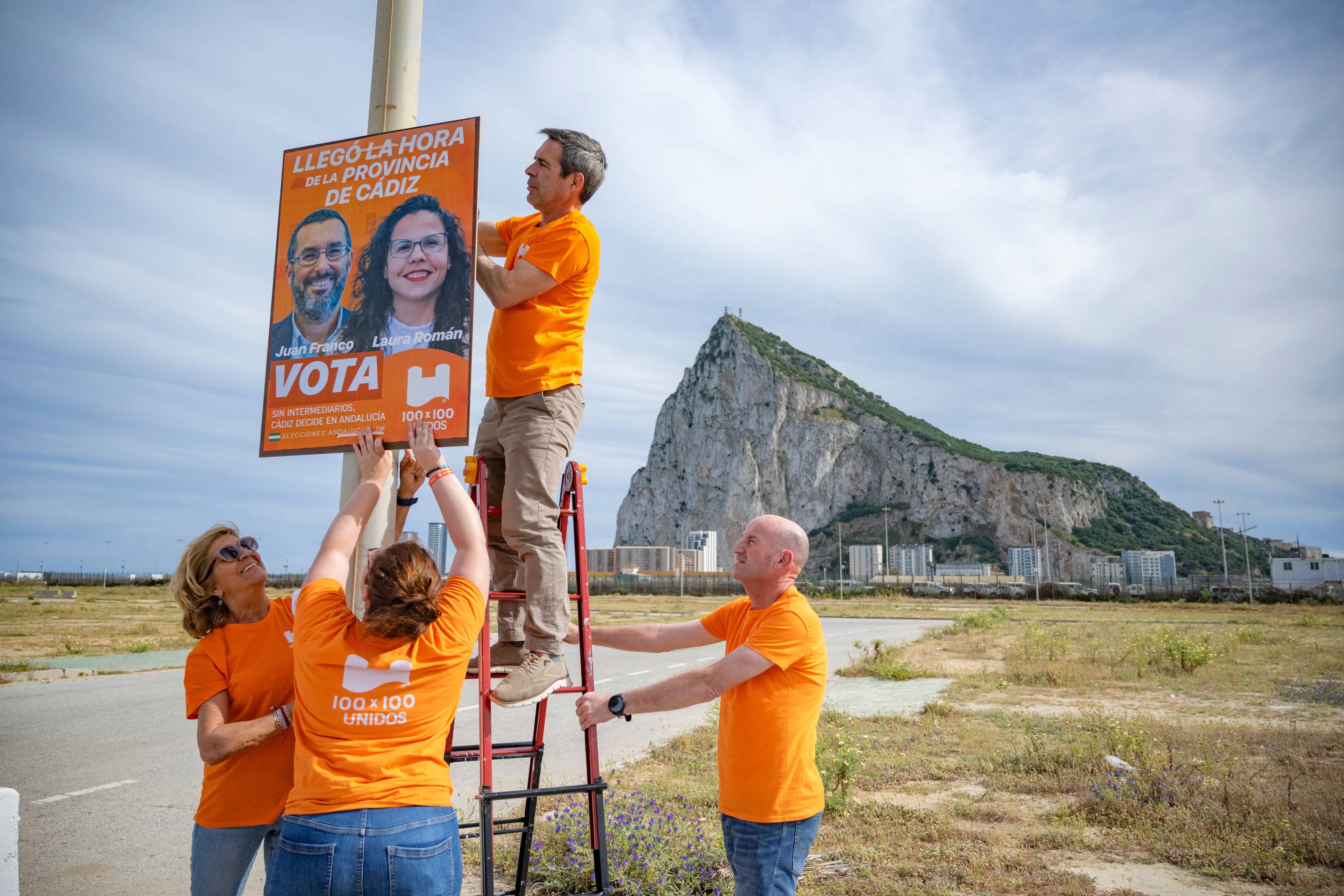 Un grupo de personas coloca un cartel del partido 100x100 Unidos en las inmediaciones de la frontera con Gibraltar.