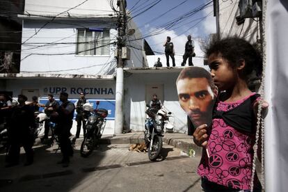 Una niña sostiene una careta con la cara de Amarildo frente a varios agentes de la Policía Pacificadora en la favela la Rocinha durante un entierro simbólico realizado el pasado 2 de noviembre en la sede de la Unidad de Policía Pacificadora donde el hombre fue supuestamente torturado y asesinado.