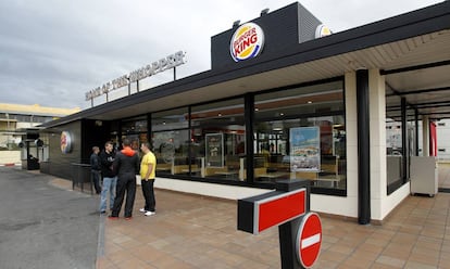 Tres j&oacute;venes conversan en la entrada de un Burger King en Coslada.