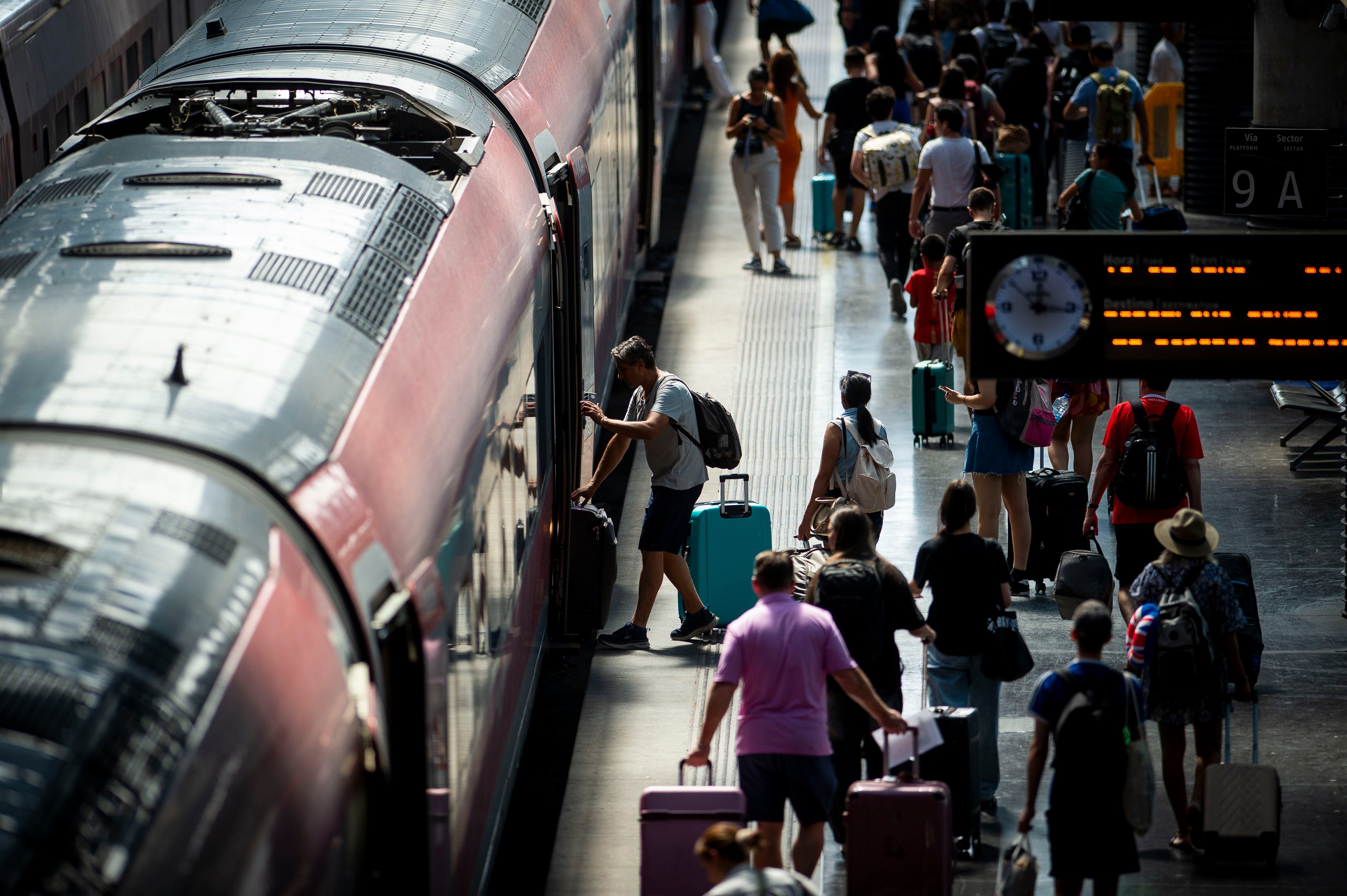 Viajeros en un andén de la estación madrileña Puerta de Atocha junto a un tren de Iryo.