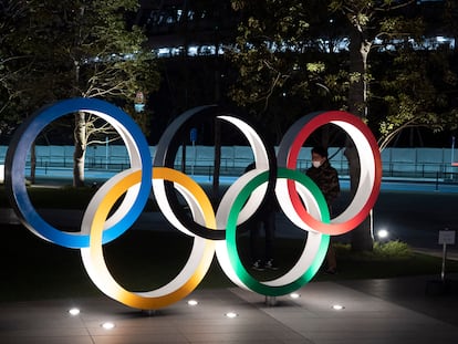 Dos hombres charlan tras los aros olímpicos junto al Nuevo Estadio Nacional en Tokio