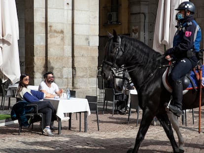 Un agente pasa a caballo junto a los clientes de una terraza de la Plaza Mayor de Madrid, que no llevan la mascarilla obligatoria.