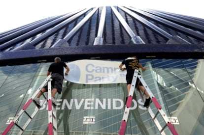 Dos operarios colocan los vinilos de la Campus Party en la puerta principal del Ágora.