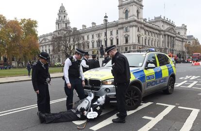 Un activista del cambio climático vestido como el cómico Charlie Chaplin conversa con agentes de policía tras bloquear el tráfico fuera del Palacio de Westminster, en Londres (Reino Unido).