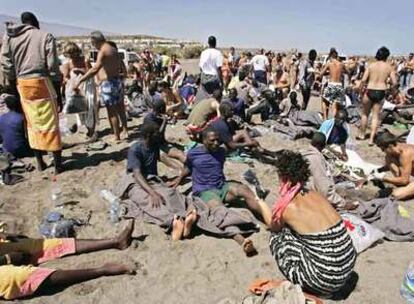 Turistas e inmigrantes, que acaban de llegar en una patera, se mezclan en la playa de Tejita, en Granadilla (Tenerife).