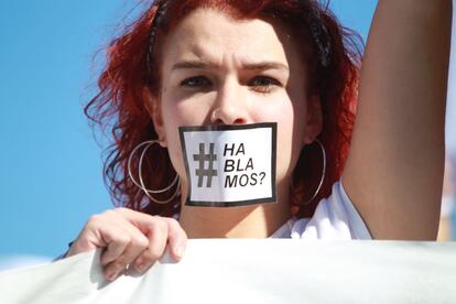 Una joven se tapa la boca con una pegatina con el lema "#Hablamos?" en la plaza de Cibeles de Madrid.