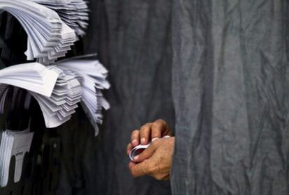 Un hombre introduce una papeleta electoral en un sobre dentro de una cabina en un colegio de Málaga.