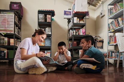 Una voluntaria lee cuentos a dos niños en una biblioteca.