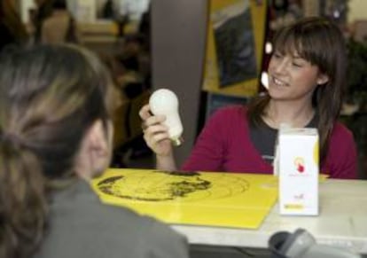 Una joven contempla una bombilla de bajo consumo en la oficina central de Correos de Zaragoza. EFE/Archivo