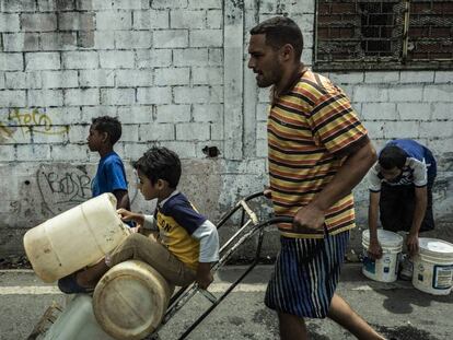 Pai e filhos carregam galões de água em Caracas