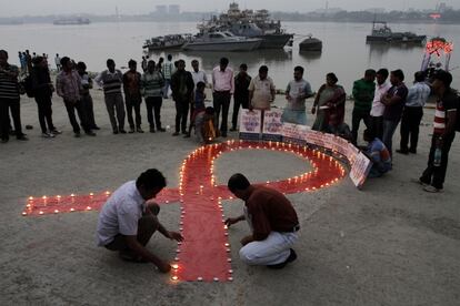 Dos personas encienden velas para rodear un lazo rojo gigante colocado en una de las orillas del r&iacute;o Ganges en India.