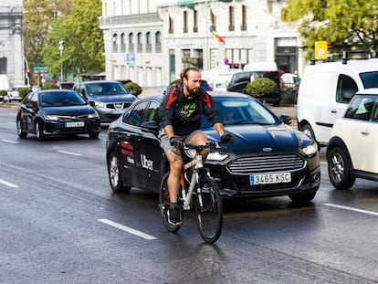 Un coche de Uber pasa a pocos centímetros de un ciclista por la calle Alcalá de Madrid, este lunes.