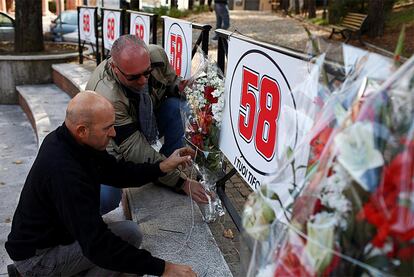 Dos aficionados depositan flores junto a un cartel con el número '58', el que lucía el piloto en su moto.