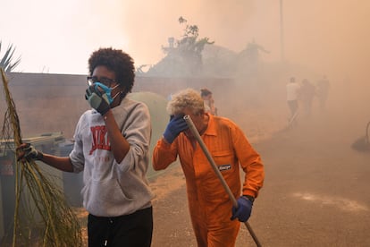 Dos personas que colaboran en las tareas de extinción se alejan de un foco del incendio en Veiga das Meas, este sábado.