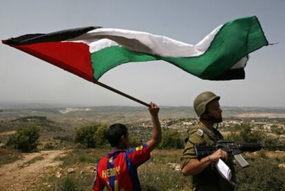 Un joven palestino ondea una bandera nacional al lado de un policía fronterizo israelí hoy en el poblado de Beit Omar en Cisjordania